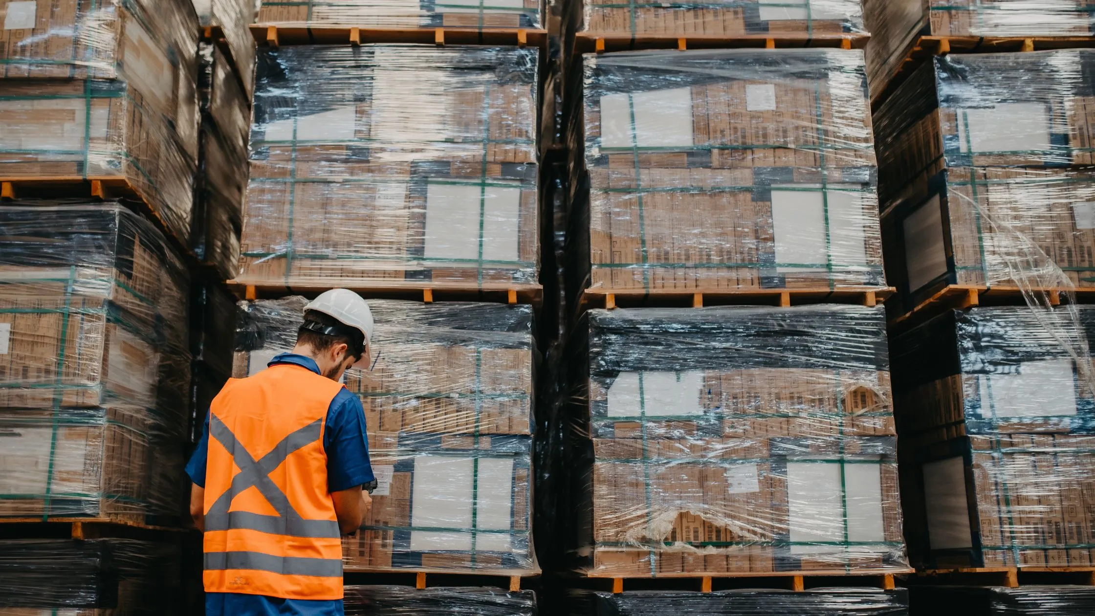A warehouse operative checking shrink-wrapped pallets in a distribution centre